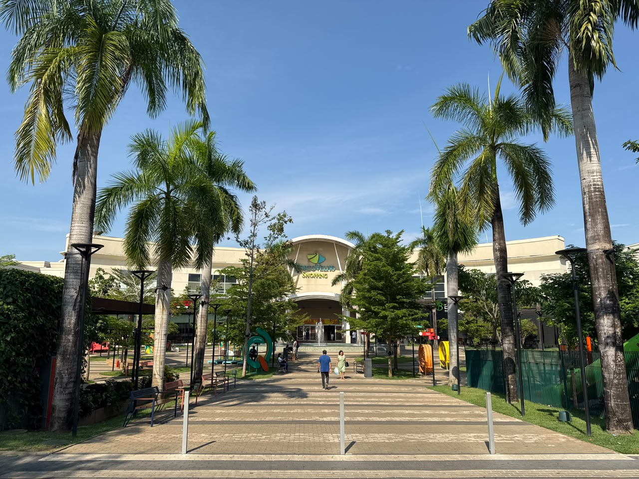 Fachada e área de convivência do Porto Velho Shopping, com caminho ladeado por palmeiras